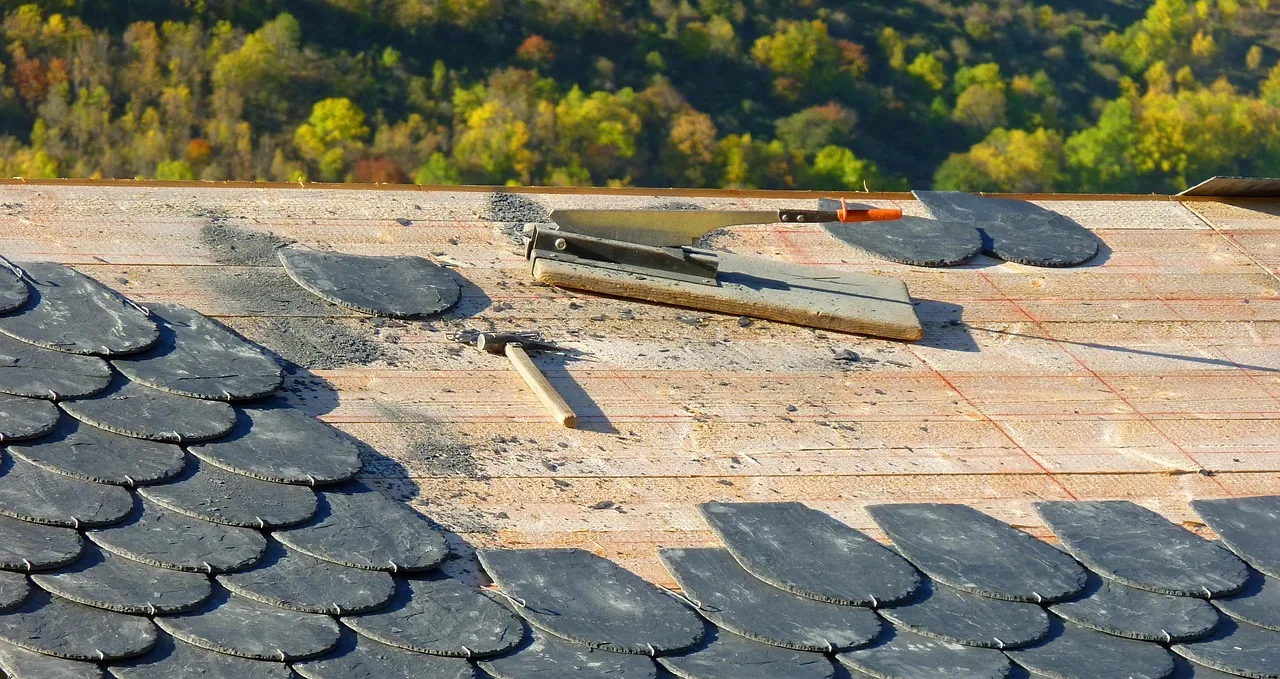 Schieferdach in Arbeit: halb gedeckte Schieferschuppen auf der Schalung, daneben Schieferhammer und Haubrücke
